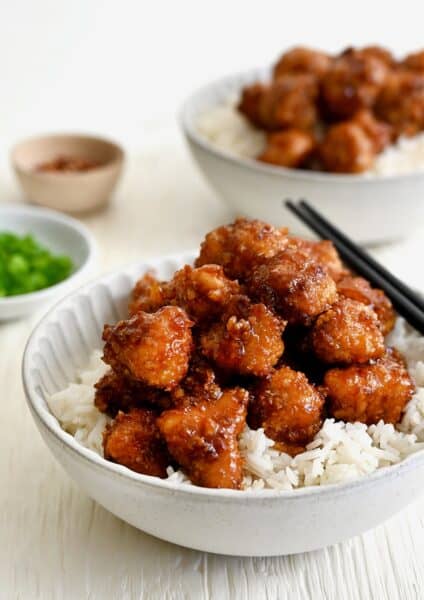 Baked Orange Chicken atop white rice in a bowl with chopsticks.