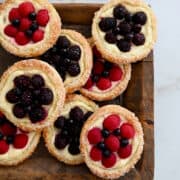 Easy cream cheese danish with fresh berries piled atop a wood serving board with bowls containing fresh berries in the background.