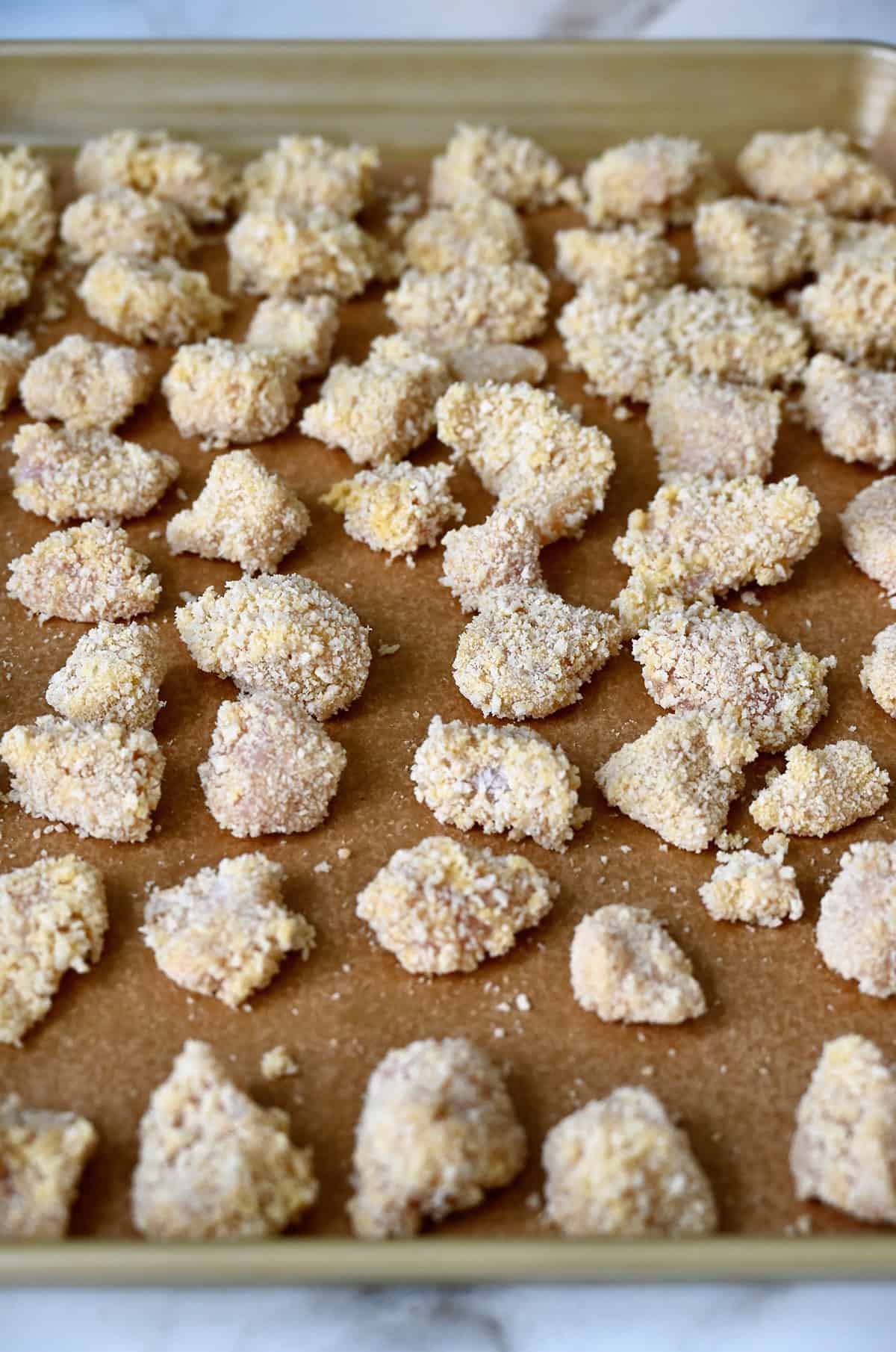 Breaded chicken pieces on a parchment paper-lined baking sheet.