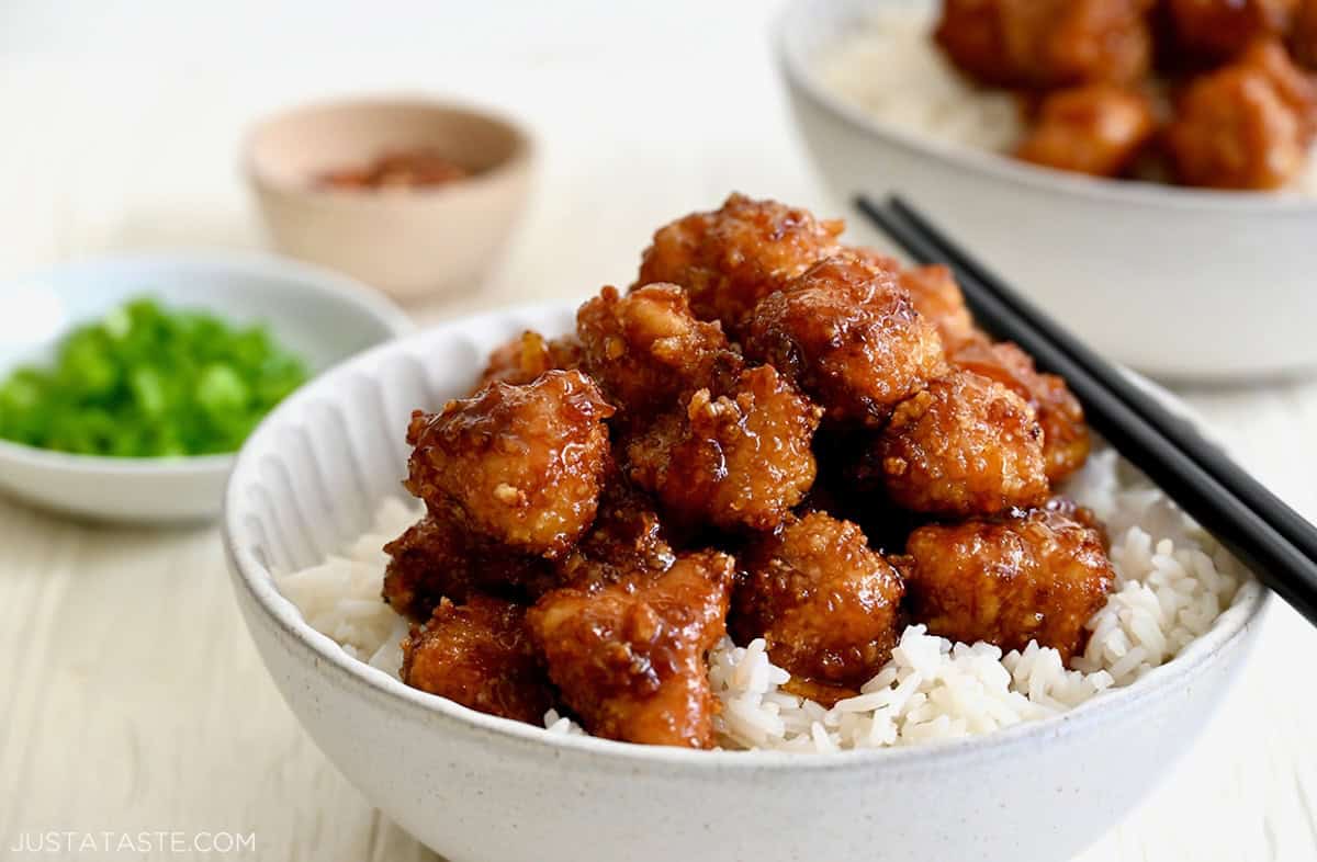 Copycat Panda Express baked orange chicken atop steamed jasmine rice in a white bowl. 