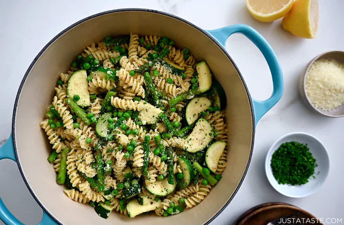 Garlicky Pasta Primavera in a large stockpot next to small bowls containing chopped fresh chives and Parmesan cheese, plus a lemon cut in half