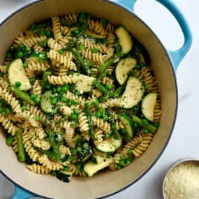 A top-down view of a large stockpot containing Garlicky Pasta Primavera, including peas, sliced zucchini and asparagus