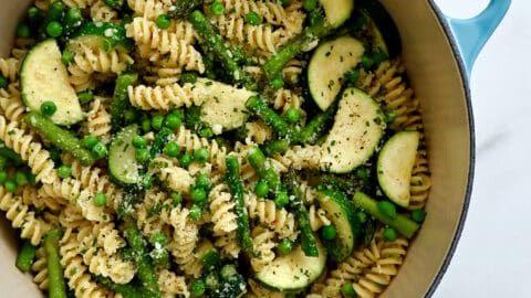 A top-down view of a large stockpot containing Garlicky Pasta Primavera, including peas, sliced zucchini and asparagus