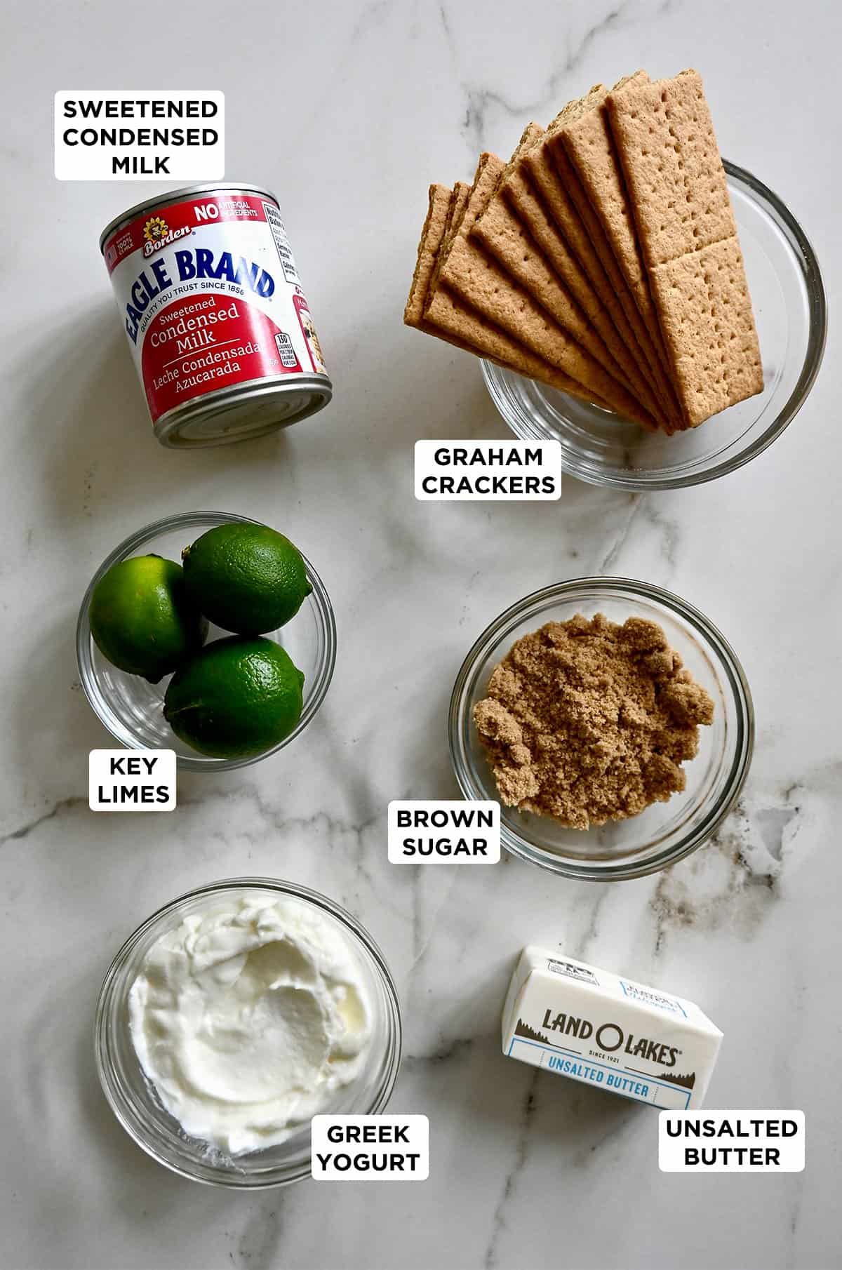 Key lime pie ingredients, including sweetened condensed milk, key limes, Greek yogurt, butter, brown sugar and graham crackers.