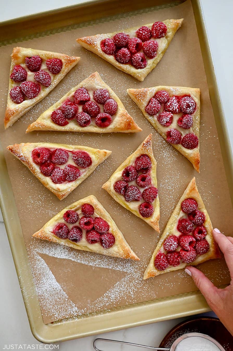 A hand reaches for a raspberry and cream cheese danish