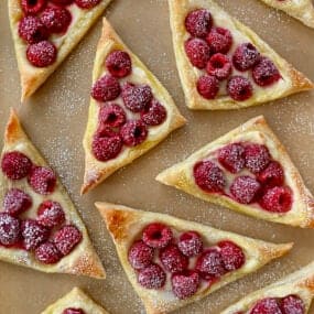 A top-down view of Raspberry Cream Cheese Danish dusted with powdered sugar atop brown parchment paper