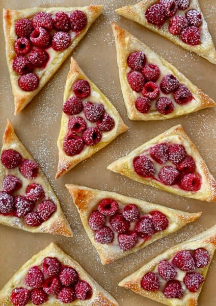 A top-down view of Raspberry Cream Cheese Danish dusted with powdered sugar atop brown parchment paper