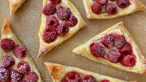 A top-down view of Raspberry Cream Cheese Danish dusted with powdered sugar atop brown parchment paper