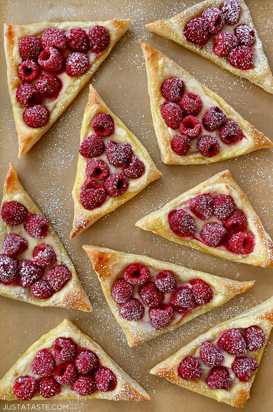 A top-down view of Raspberry Cream Cheese Danish dusted with powdered sugar atop brown parchment paper