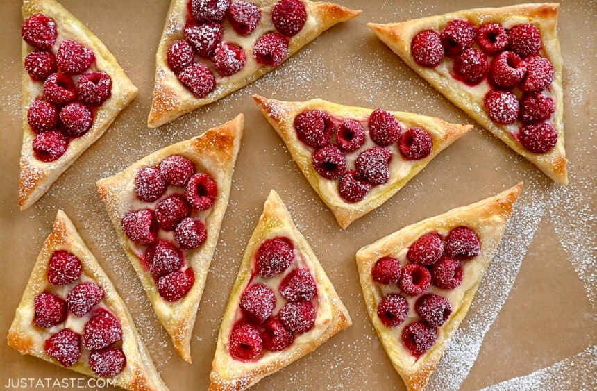 Raspberry cream cheese pastries dusted with confectioners' sugar on brown parchment paper
