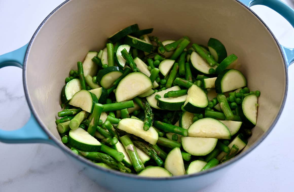 A large stockpot containing sautéed asparagus, zucchini and peas