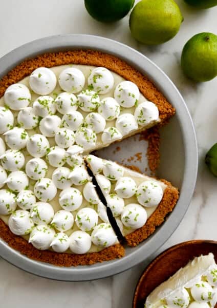 Key lime pie with a graham cracker crust topped with dollops of whipped cream and zest of a lime.