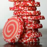 A tall stack of pink and white pinwheel sugar cookies studded with heart-shaped sprinkles.