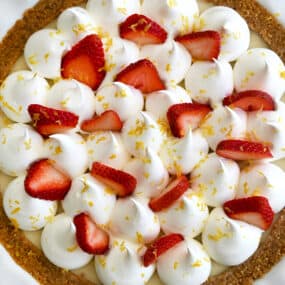 A close up of an icebox pie topped with whipped cream, strawberries and lemon zest