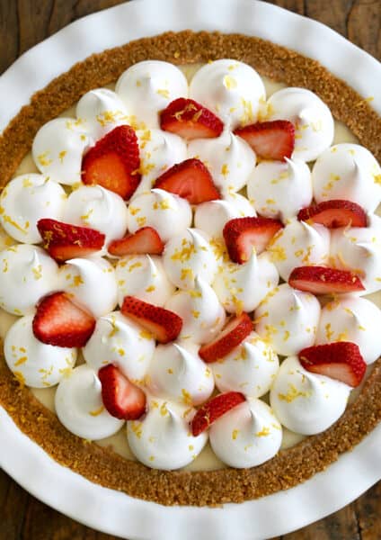 A close up of an icebox pie topped with whipped cream, strawberries and lemon zest