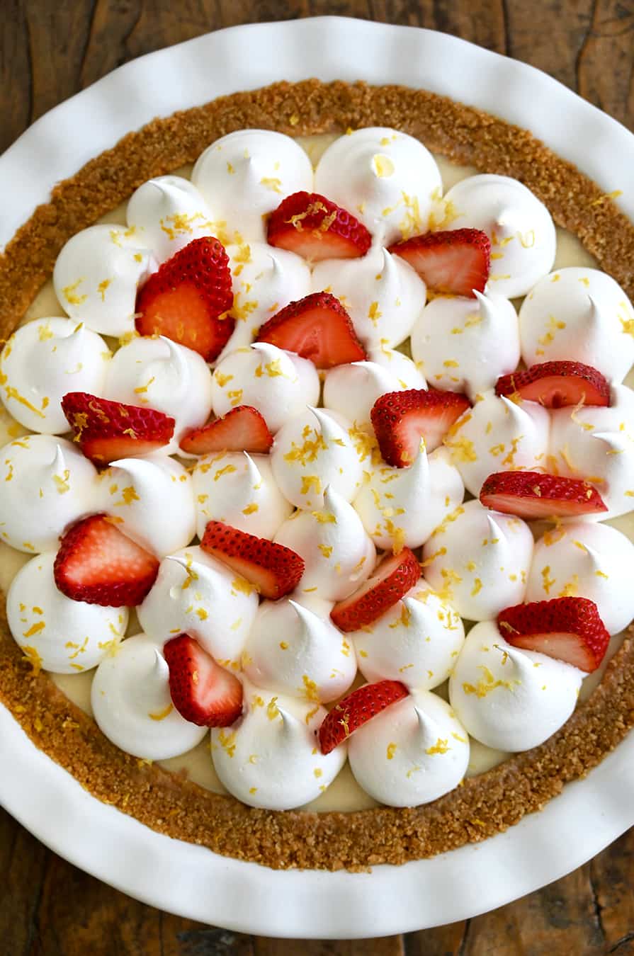 A close up of an icebox pie topped with whipped cream, strawberries and lemon zest
