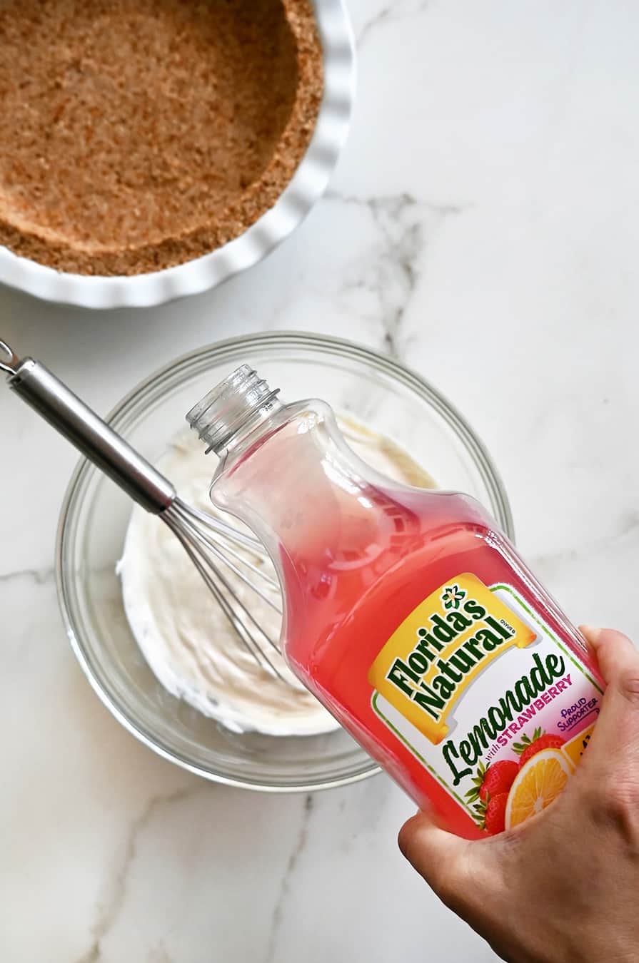 A bottle of strawberry lemonade being poured into a glass bowl