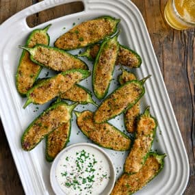 A top-down view of Air Fryer Jalapeno Poppers on a white serving plate next to a small bowl filled with Ranch dressing