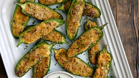 A top-down view of Air Fryer Jalapeno Poppers on a white serving plate next to a small bowl filled with Ranch dressing