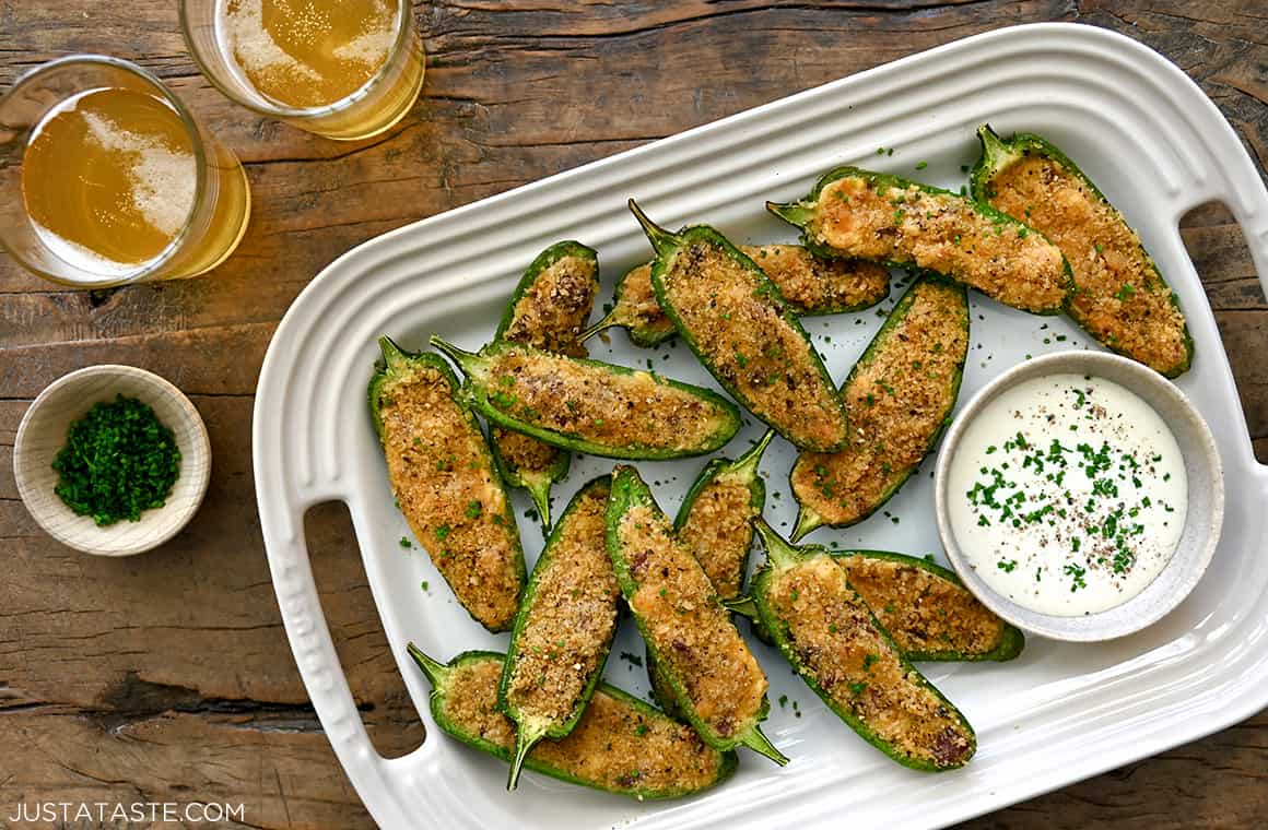 A top-down view of two glasses of beer next to a white serving platter piled high with Air Fryer Jalapeño Poppers with Bacon and a small bowl containing Ranch dipping sauce