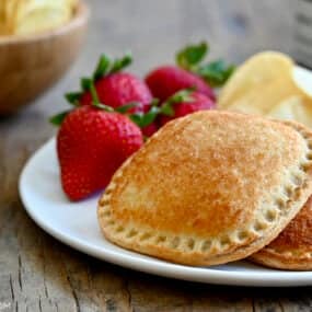 A toasted peanut butter and jelly sandwich on a white plate with strawberries and potato chips