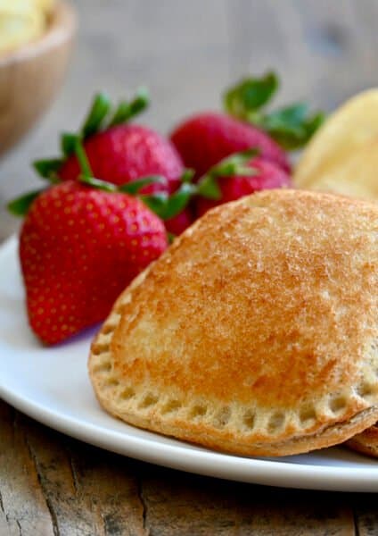 A toasted peanut butter and jelly sandwich on a white plate with strawberries and potato chips