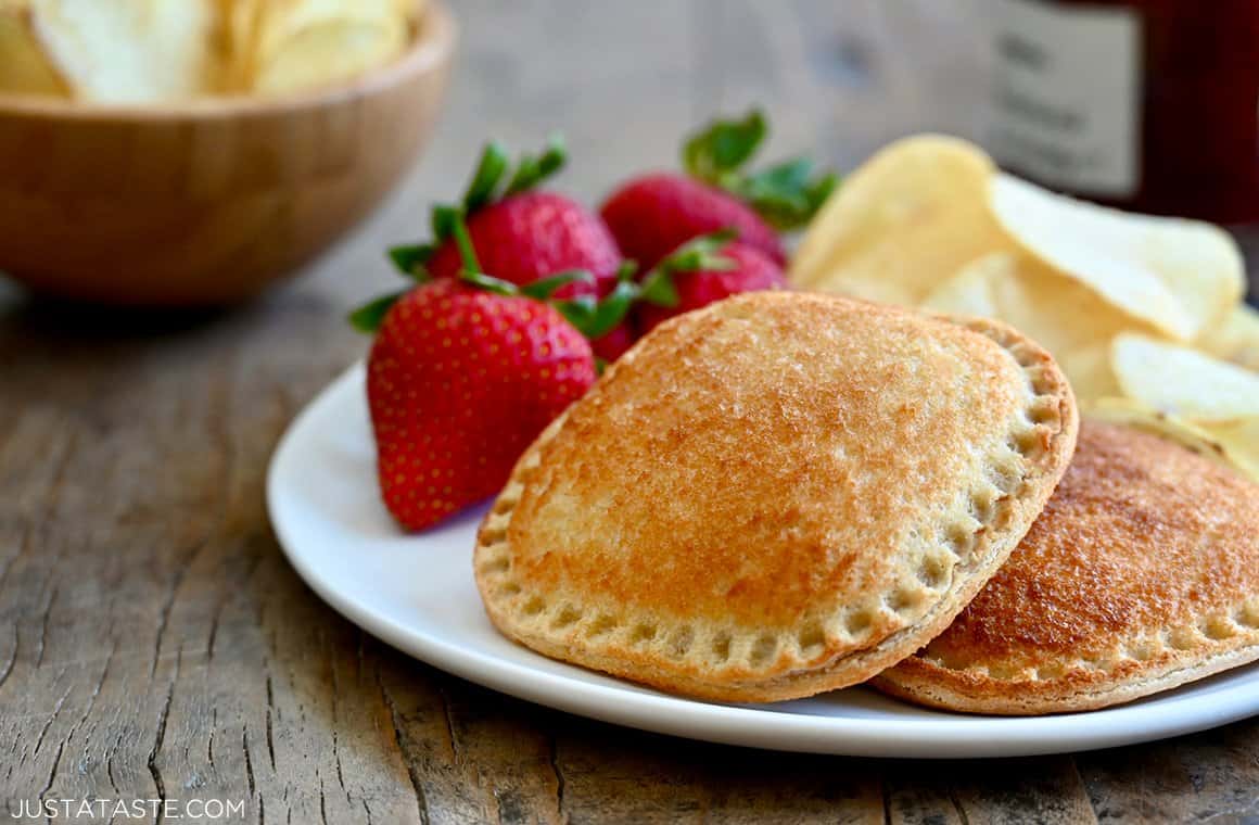 A toasted peanut butter and jelly sandwich on a white plate with strawberries and potato chips