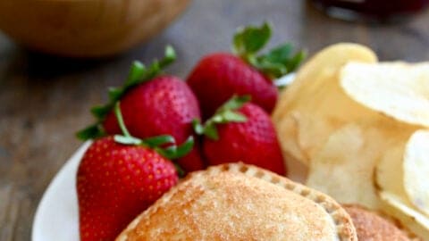 Air Fryer Peanut Butter and Jelly Uncrustables on a white plate with strawberries and potato chips