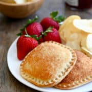 Two Air Fryer Peanut Butter and Jelly Uncrustables sandwiches on a white plate with strawberries and potato chips