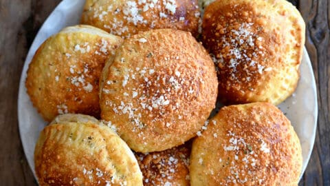 A top down view of a white plate containing air fryer pizza pockets surrounded by bowls of Parmesan and marinara sauce