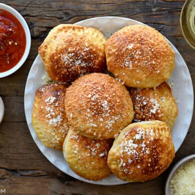 A plate containing pizza pockets surrounded by glasses of wine and small bowls of marinara and Parmesan cheese