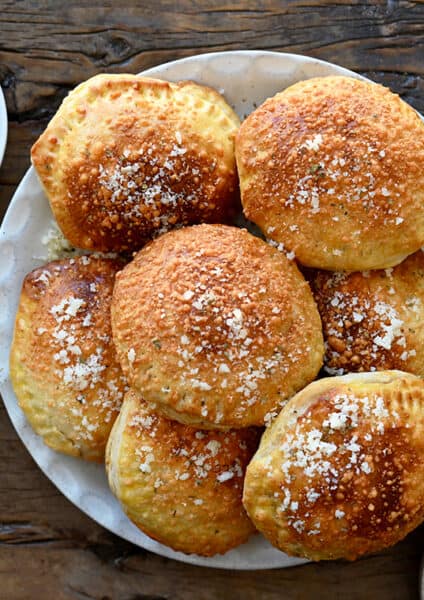 A plate containing pizza pockets surrounded by glasses of wine and small bowls of marinara and Parmesan cheese