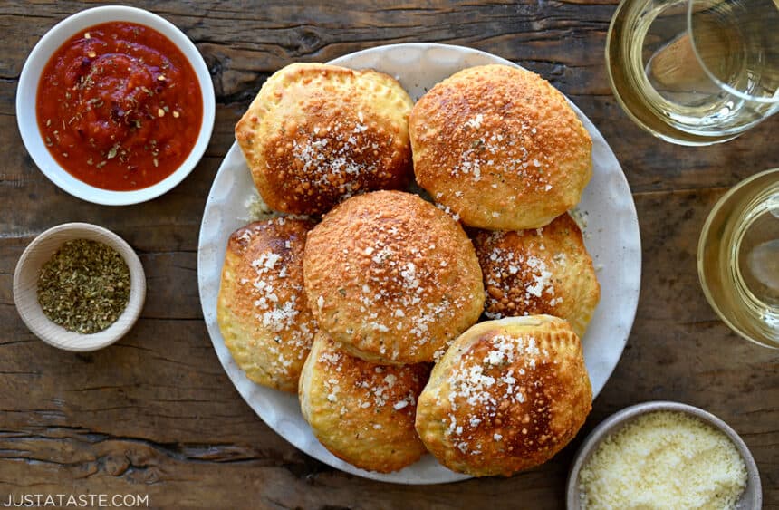 A plate containing pizza pockets surrounded by glasses of wine and small bowls of marinara and Parmesan cheese