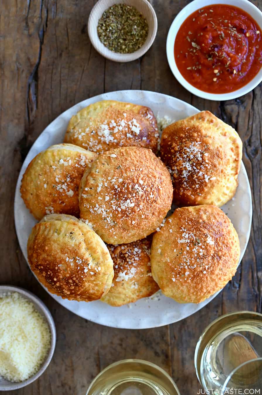 A top down view of a white plate containing air fryer pizza pockets surrounded by bowls of Parmesan and marinara sauce