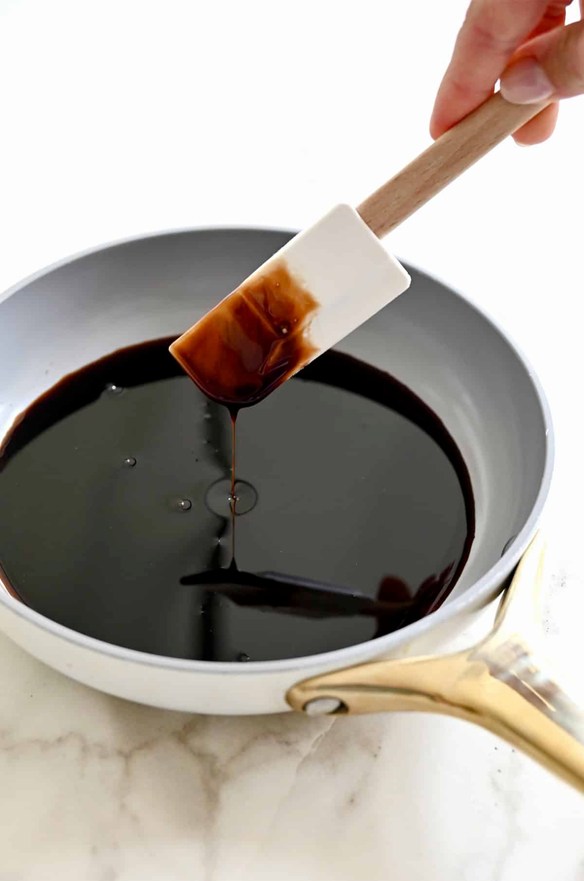 A spatula is being lifted above a skillet containing thick and syrupy balsamic syrup.
