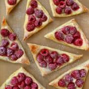 A top-down view of Cream Cheese Danishes topped with fresh raspberries and dusted with powdered sugar.