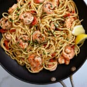 A top-down view of a nonstick skillet containing shrimp scampi pasta garnished with fresh parsley.