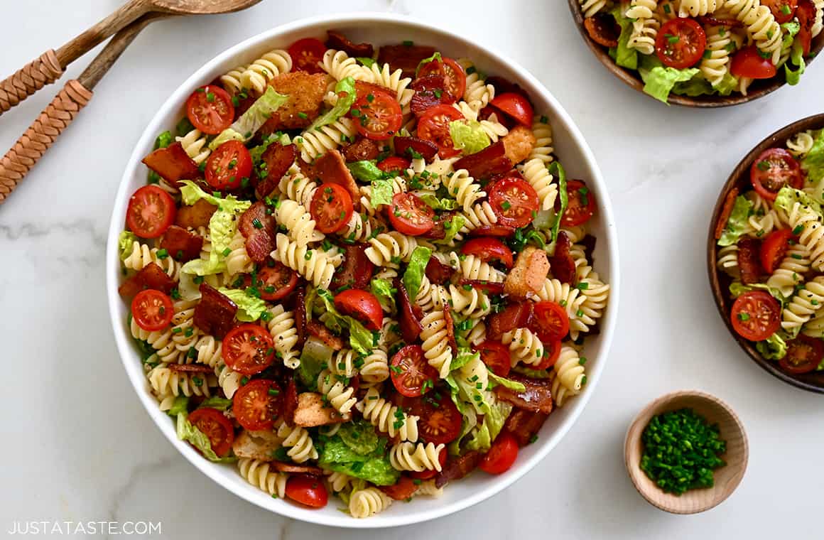A large white serving bowl containing BLT Pasta Salad starring chopped bacon, halved cherry tomatoes, lettuce and rotini noodles