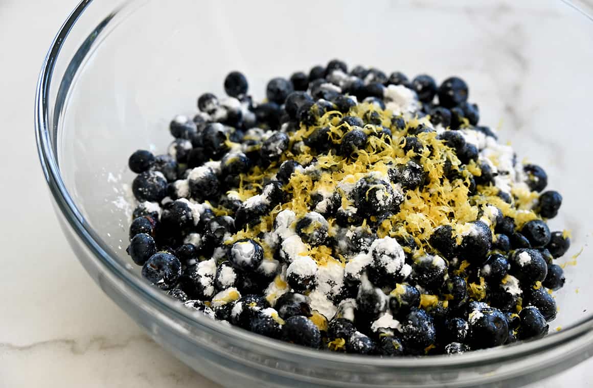 A clear bowl containing fresh blueberries, cornstarch and lemon zest