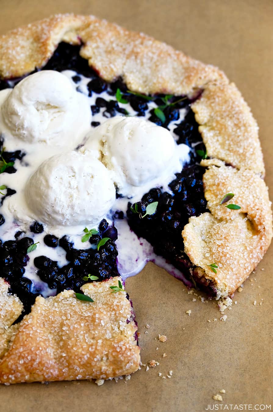 A close-up view of a homemade blueberry galette topped with three scoops of vanilla ice cream and garnished with fresh thyme