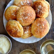 A top-down view of air fryer pizza pockets piled on a white plate next to a small bowl filled with pizza sauce and a small bowl filled with grated parmesan cheese.