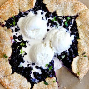 A top-down view of a Blueberry Galette topped with three scoops of vanilla bean ice cream and fresh thyme
