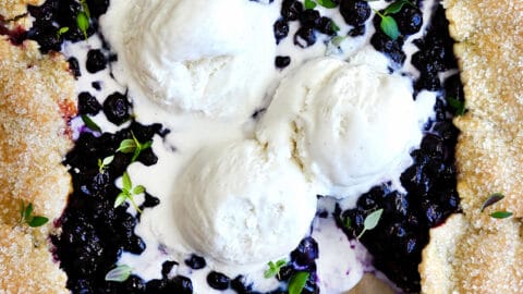 A top-down view of a Blueberry Galette topped with three scoops of vanilla bean ice cream and fresh thyme