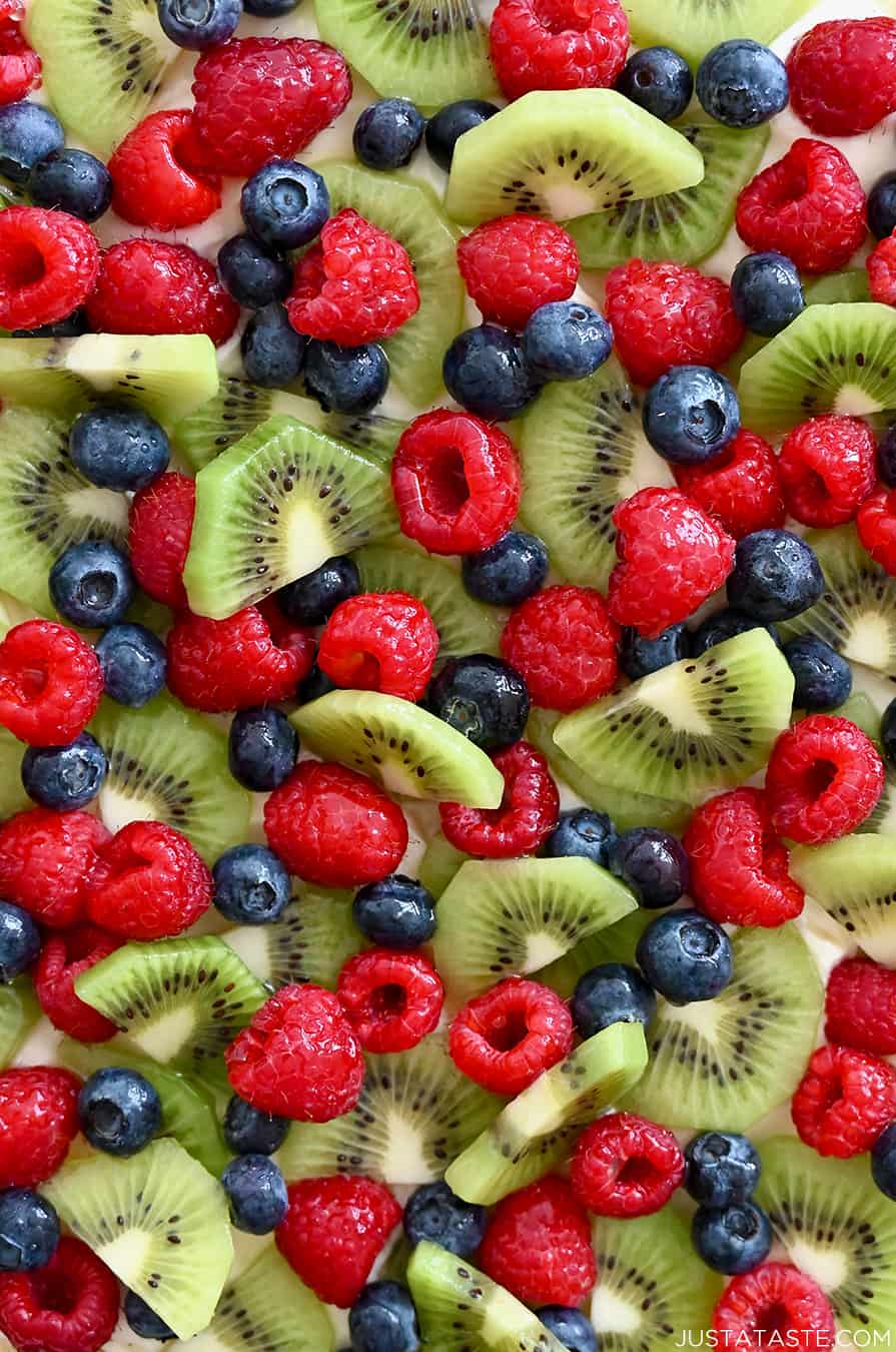 A close-up view of fresh raspberries, blueberries and sliced kiwi atop cream cheese frosting