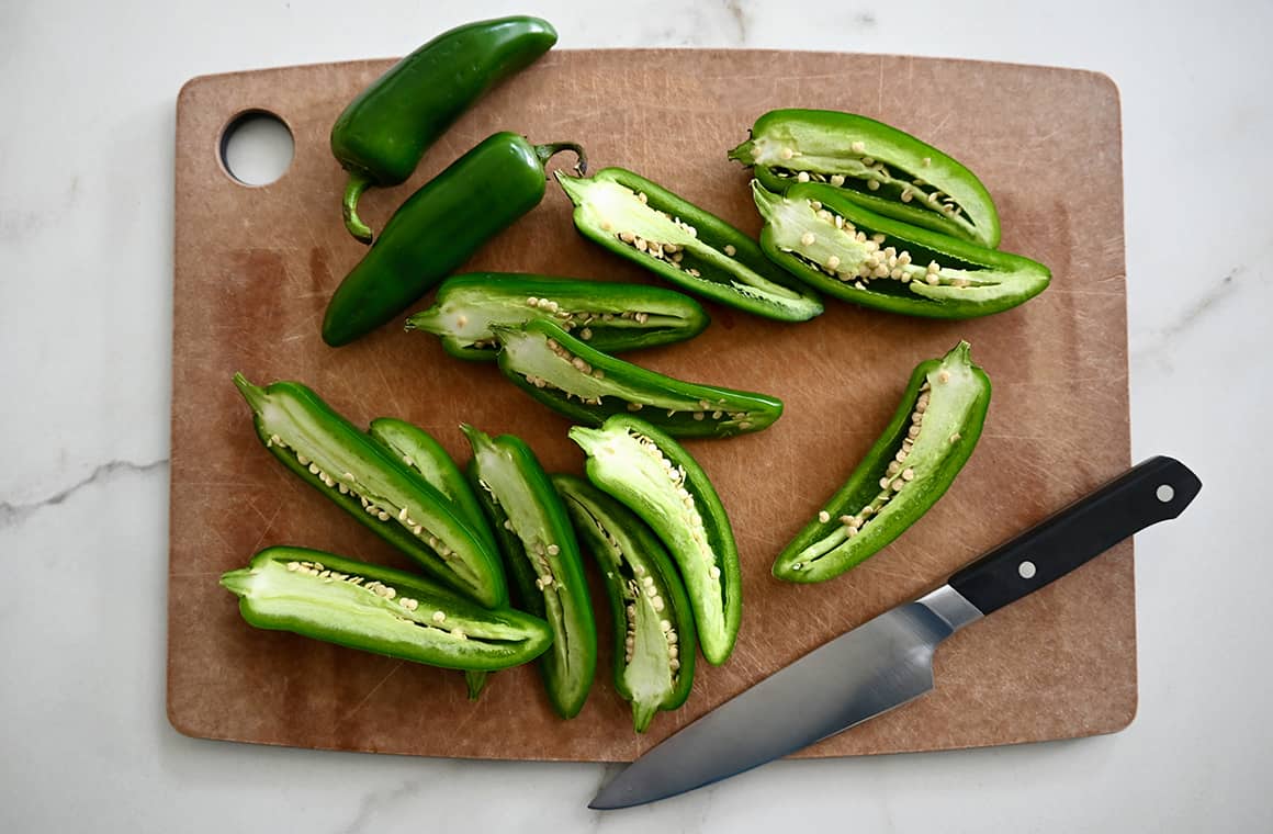 Halved jalapeños on a cutting board next to a sharp knife