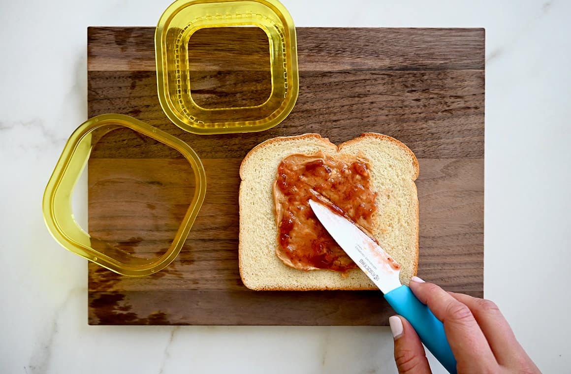 A wood cutting board with sliced bread and peanut butter and jelly