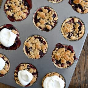 A top-down view of a muffin tin with Mini Cherry Pies with Streusel topped with homemade whipped cream