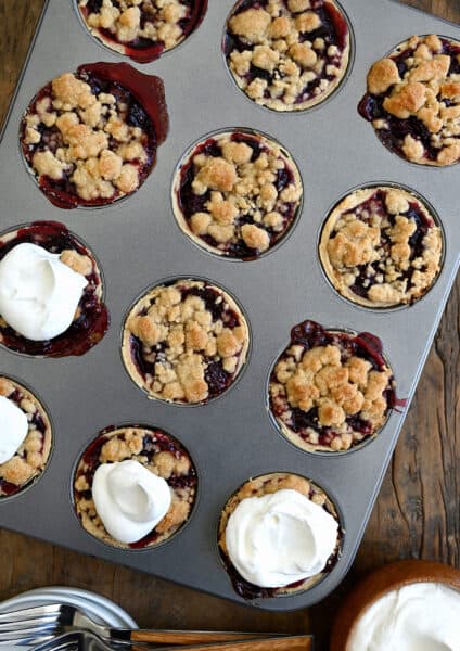 A top-down view of a muffin tin with Mini Cherry Pies with Streusel topped with homemade whipped cream