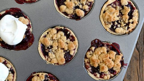 A top-down view of a muffin tin with Mini Cherry Pies with Streusel topped with homemade whipped cream