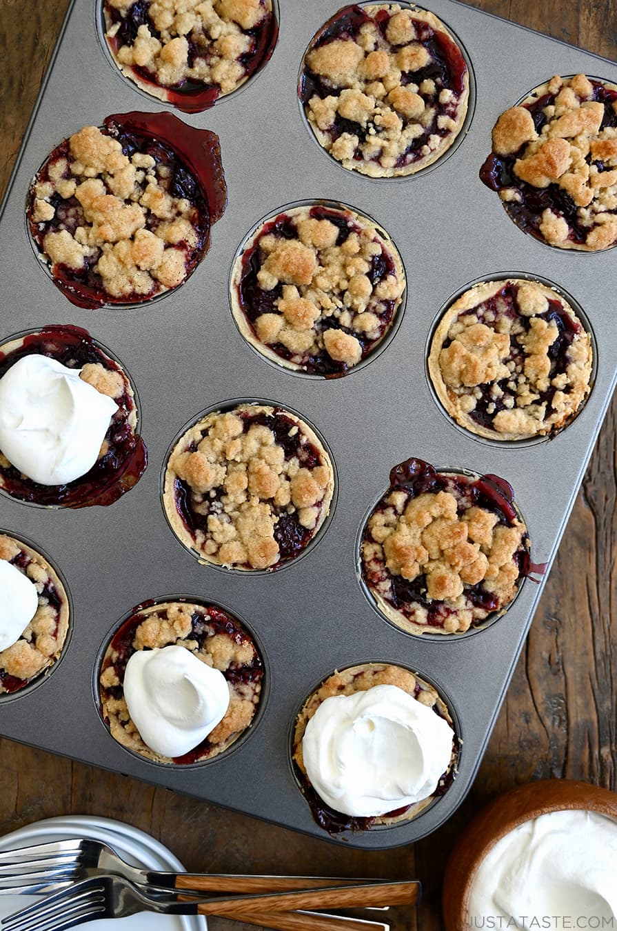 A top-down view of a muffin tin with Mini Cherry Pies with Streusel topped with homemade whipped cream